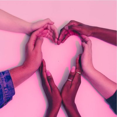 Four hands of different skin tones forming a heart shape against a pink background