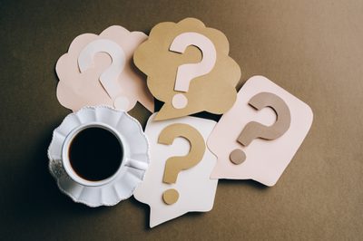 Paper question marks and speech bubbles arranged around a cup of black coffee