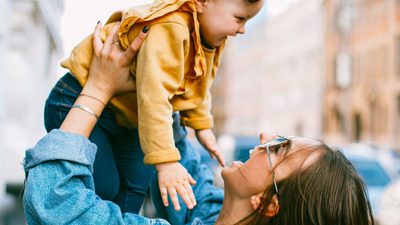 A woman lifting a laughing toddler in the air outdoors
