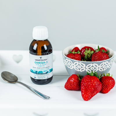 Vegetology Omega-3 unflavoured liquid bottle beside a bowl of strawberries and a teaspoon