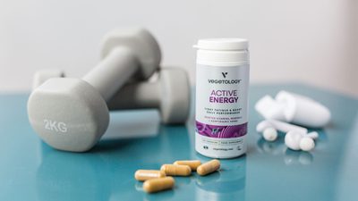 An Active Energy tub and loose capsules on a blue table beside a pair of dumbbells