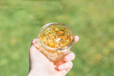 Hand holding a glass jar of vegan omega-3 capsules outdoors on a lawn