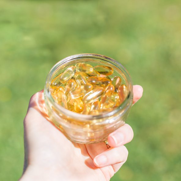 Hand holding a glass jar of vegan omega-3 capsules outdoors on a lawn
