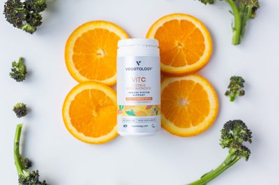 Vit C bottle in a flat-lay of orange slices and purple sprouting broccoli