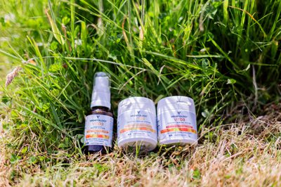 Vegetology Vit D3 spray and two supplement tubs lying in long grass