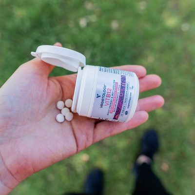 A hand tipping Vegetology Vit B12 tablets from the open tub into the palm, outdoors on grass