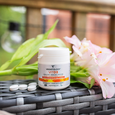A Vegetology Vit D3 2500iu tub and three tablets on a garden table beside pale pink alstroemeria flowers